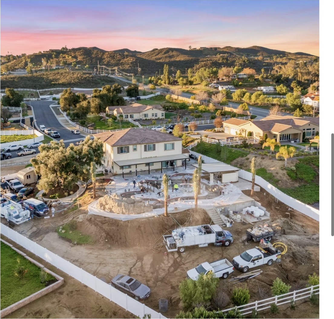 Sunset aerial of a hillside estate with the Prime Time crew plastering a large custom pool