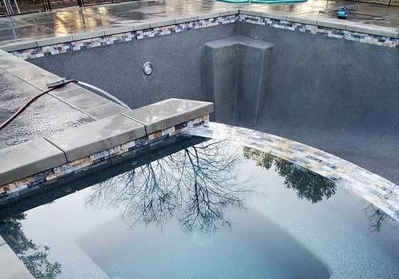 Finished pool and spa with gray plaster finish, glass tile band and spillway